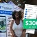 Iman Wims standing in front of a Thumzup promotional banner at an outdoor event, smiling while holding a tote bag.